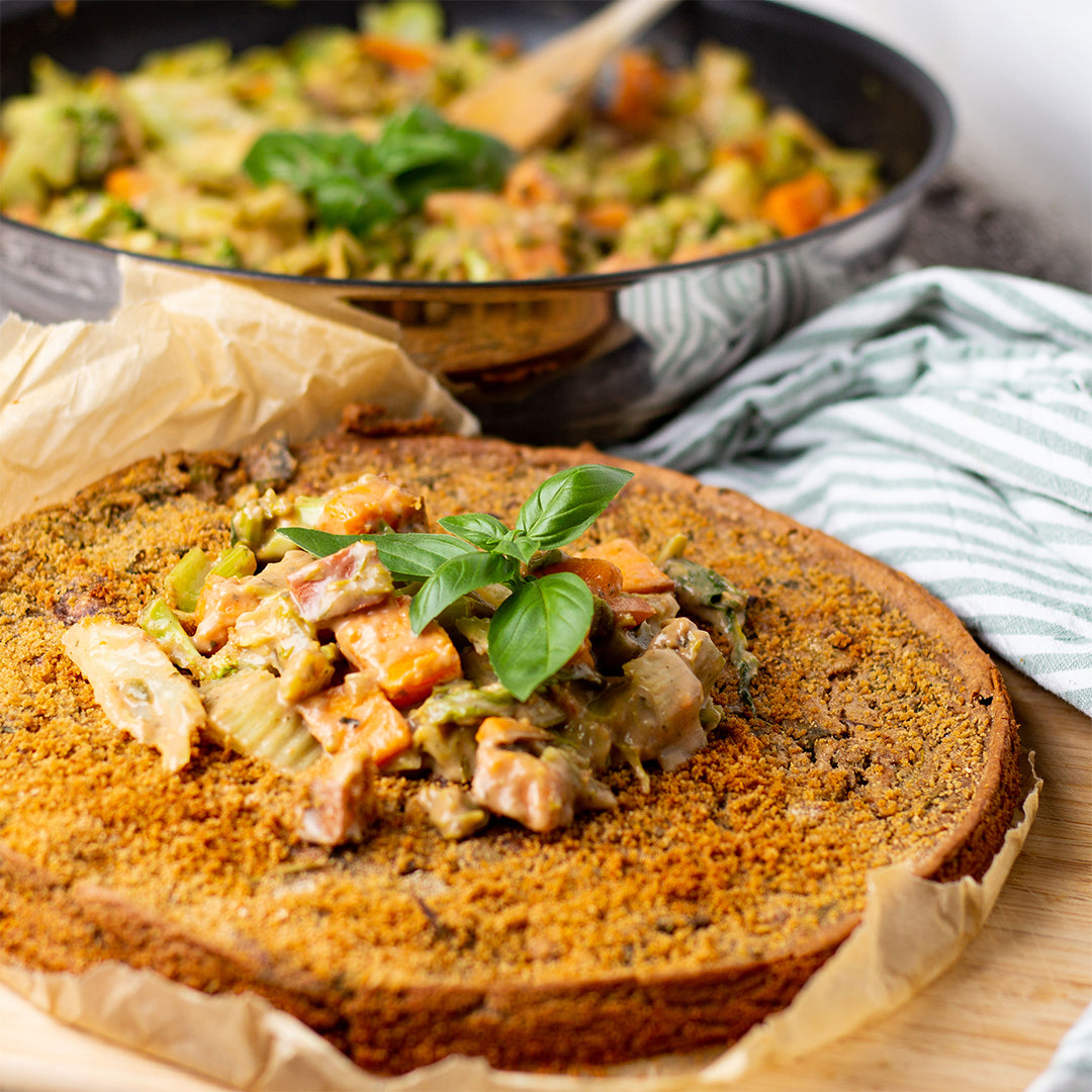 Eine italienische Farinata liegt auf Backpapier. Im Hintergrund ist eine Pfanne zu sehen.