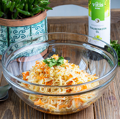 Ein Krautsalat in einer Glasschüssel mit einer Flasche Traubenkernöl von Vitis24 im Hintergrund.