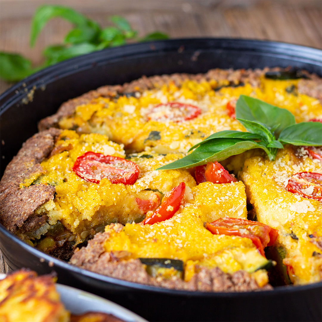 Eine Quiche mit Polenta und geschnittenen Tomaten in einer Auflaufform.