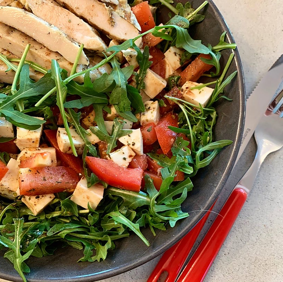 eine graue Schale mit Salat aus Rucola, Tomatenstücken und gegrillten Hähnchenstreifen
