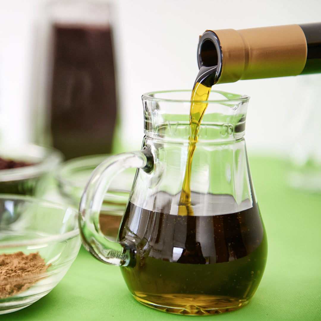 aus einer Flasche wird grüngelbes Traubenkernöl in eine Glaskaraffe gegossen