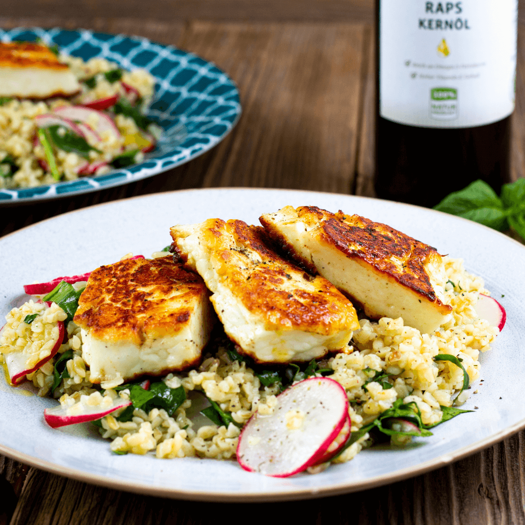 Taboulé mit Halloumi angerichtet auf einem weißen Teller mit einer Flasche Rapsöl von Vitis24 im Hintergrund. 