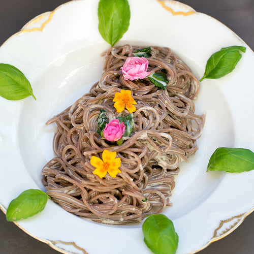 Ein Teller mit Basilikum-Zitronen-Cashewsahne an Traubenkernspaghetti dekorativ angerichtet.