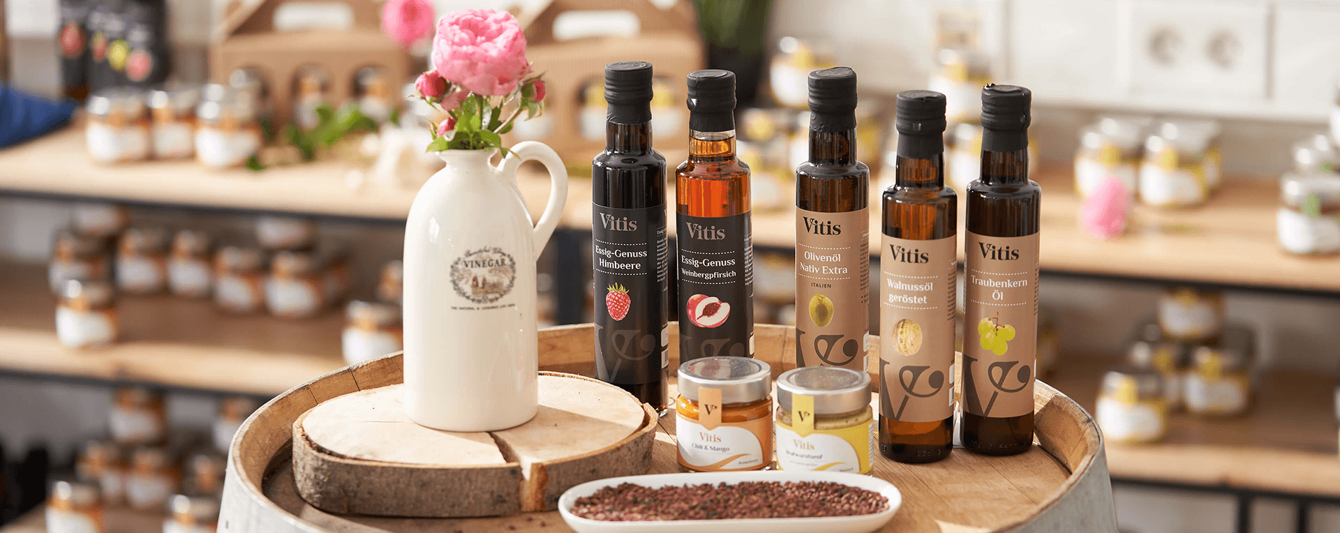 Ein Bild mit verschiedenen Speiseölen und Essigen von der Firma Vitis Traubenkern GmbH auf einem Holzfass dekoriert.