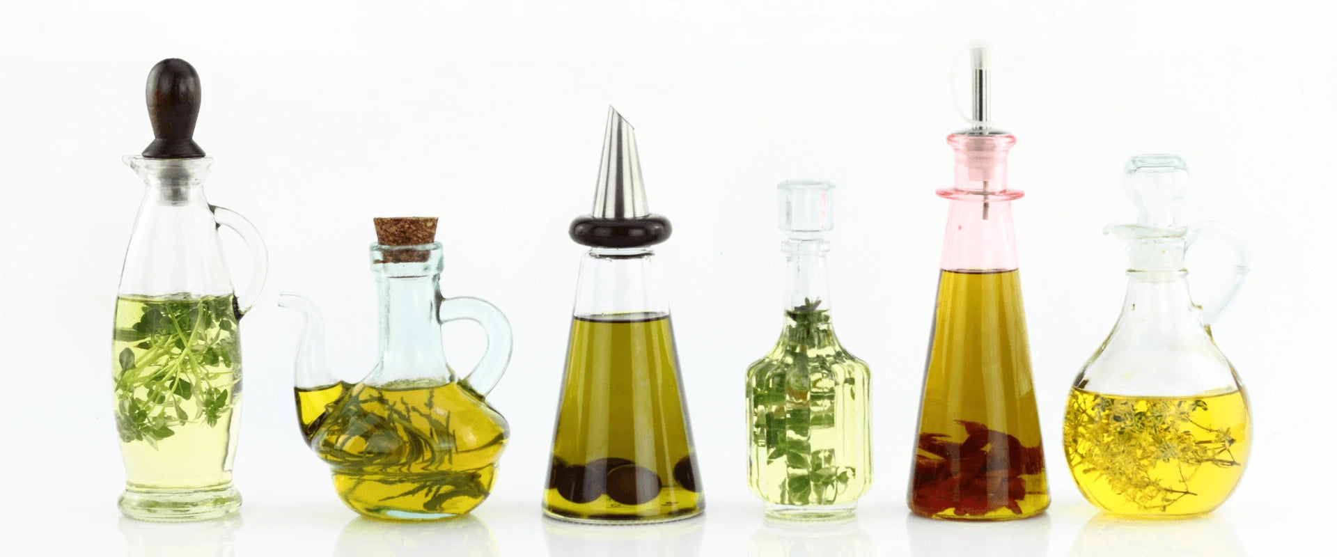 Verschiedene Speiseöle in besonders geformten Karaffen stehen auf einem hellen Untergrund.