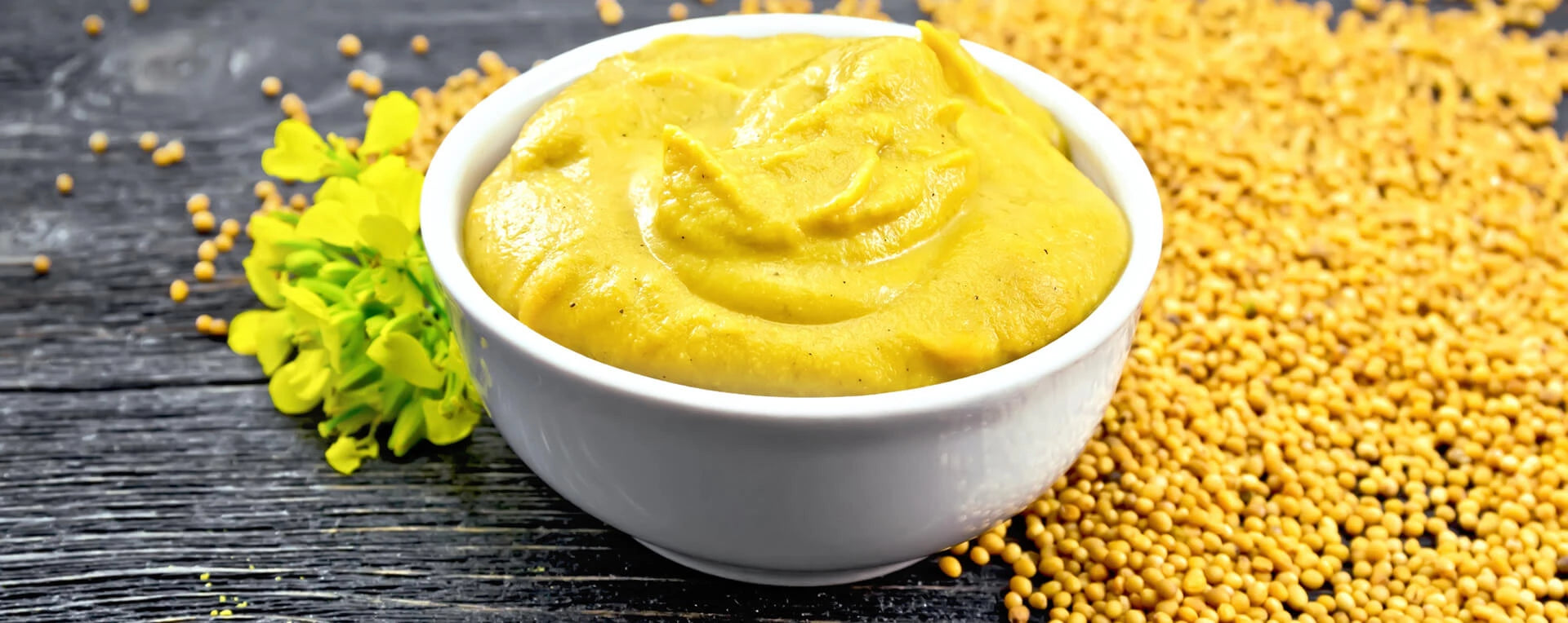 ein Schälchen Senf auf einem Tisch mit Senfkörnern als Dekoration