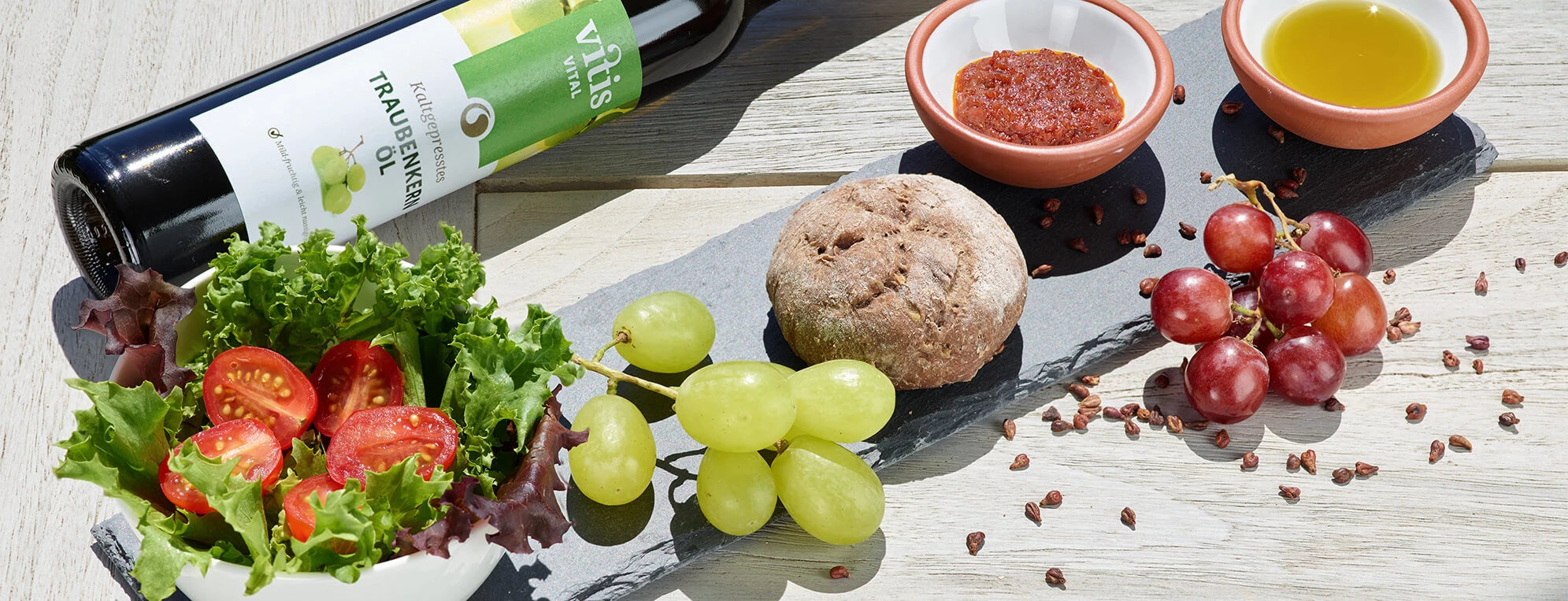 eine Flasche Traubenkernöl und ein Traubenkernbrot angerichtet mit Deko und Traubenkernen auf einem Tisch