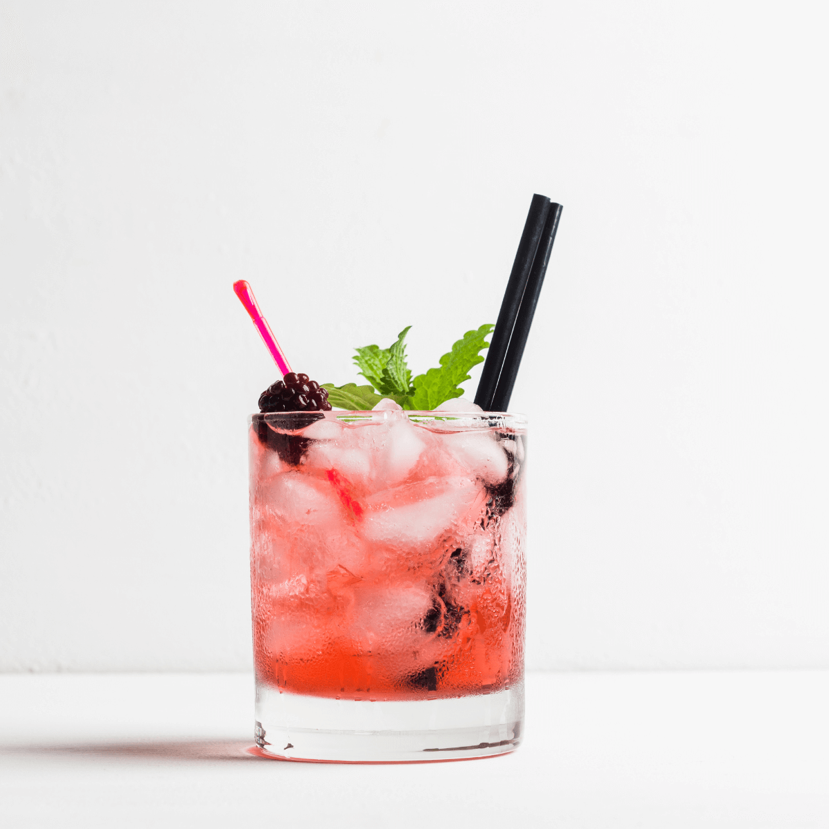 Ein fruchtig spritziger Likör in einem Tumbler Glas. Als Garnitur sind eine Brombeere und ein Minzblat zu sehen.
